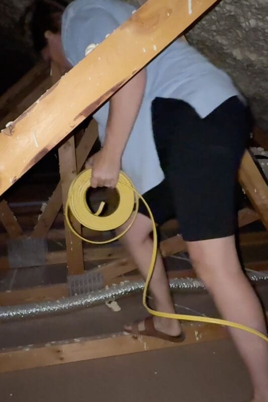 Crystel carrying a coil of yellow electrical wire through the attic trusses to run power for a DIY electric fireplace