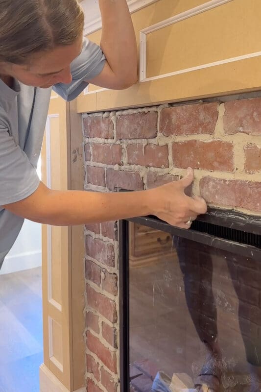 Crystel using a grout bag to pipe mortar into the gaps between the bricks on the fireplace surround, with the box molding trim above