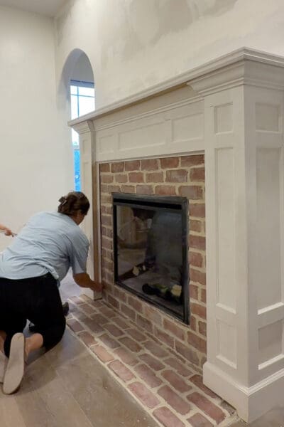 Crystel kneeling on the hearth to install trim along the inside edge of the fireplace column where the wood meets the brick surround