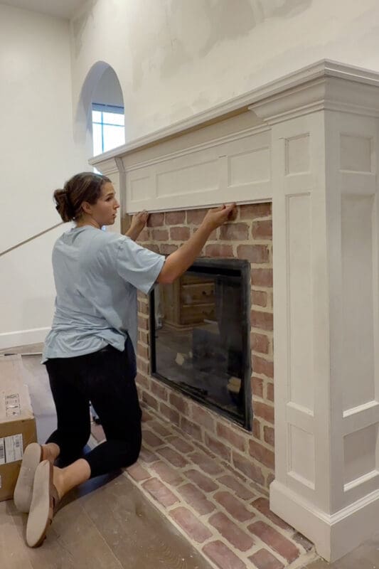 Crystel fitting a strip of trim along the bottom of the painted mantel where it meets the brick, covering the edge for a clean transition