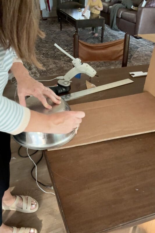 Crystel tracing around an upside-down stainless steel mixing bowl on a piece of cardboard to draw the rounded shape for the side of a cardboard trunk lid.