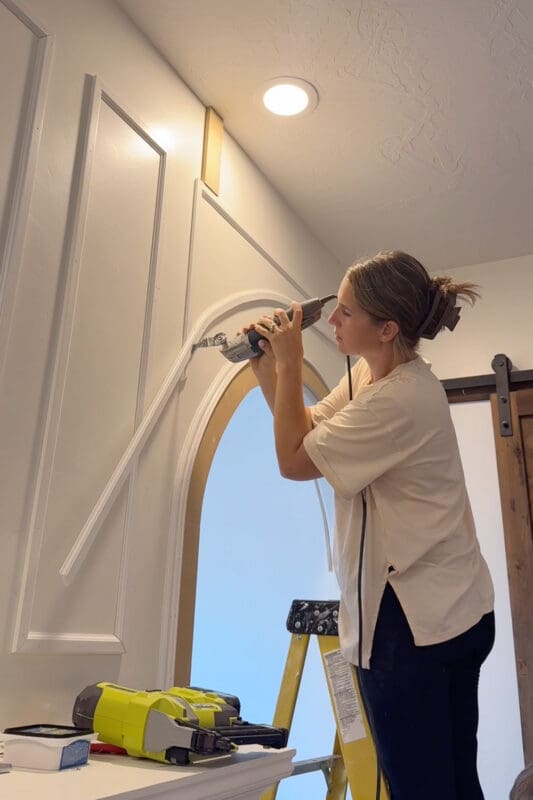 Crystel using an oscillating multi-tool to trim the end of a curved molding piece above the arch where it meets the vertical rail of the box